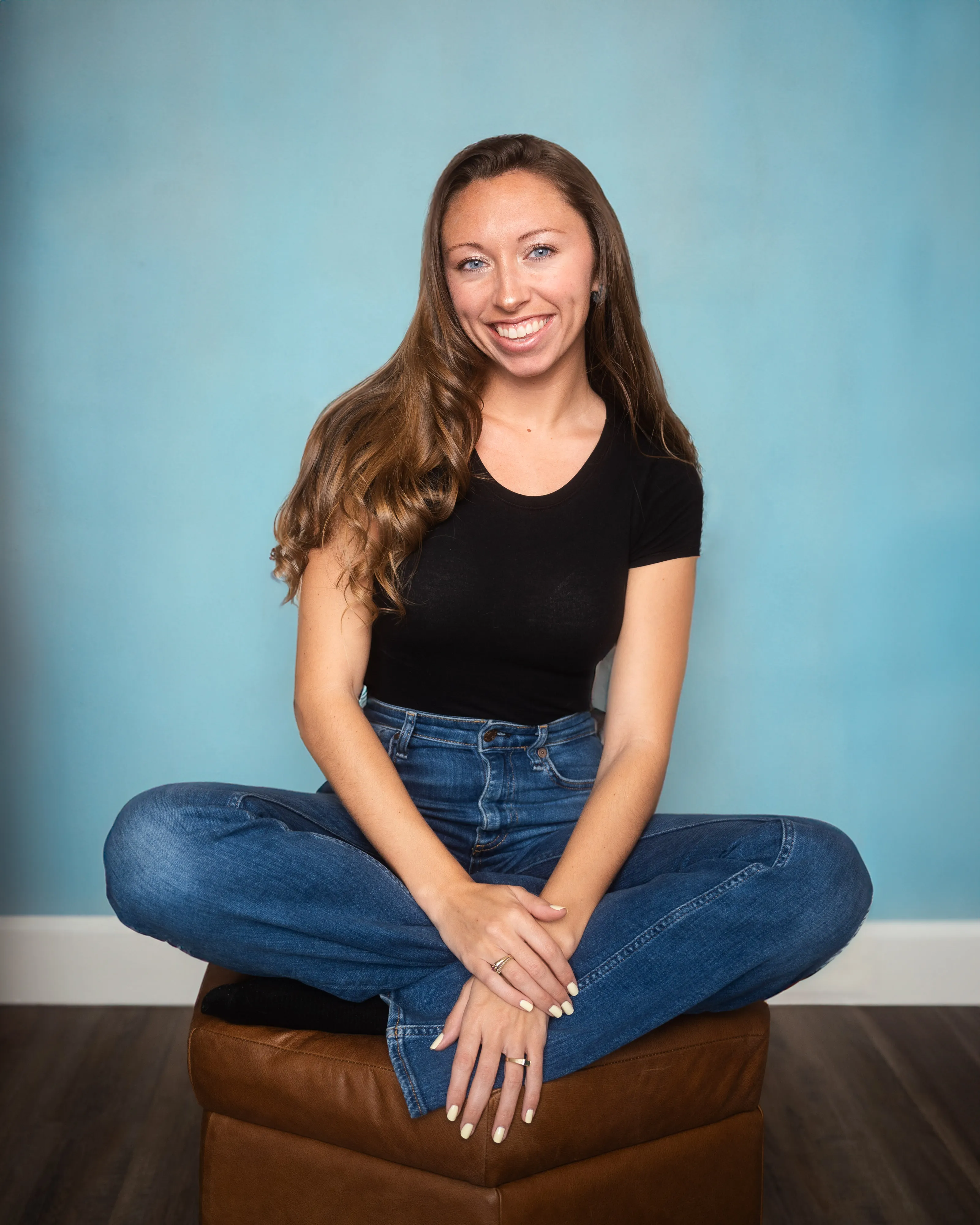 Simone Liberty smiling, sitting cross-legged in front of a blue wall